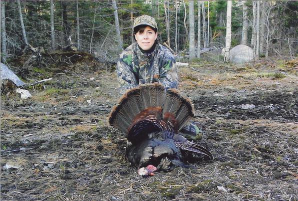 Hunter kneeling behind a harvested wild turkey in the woods